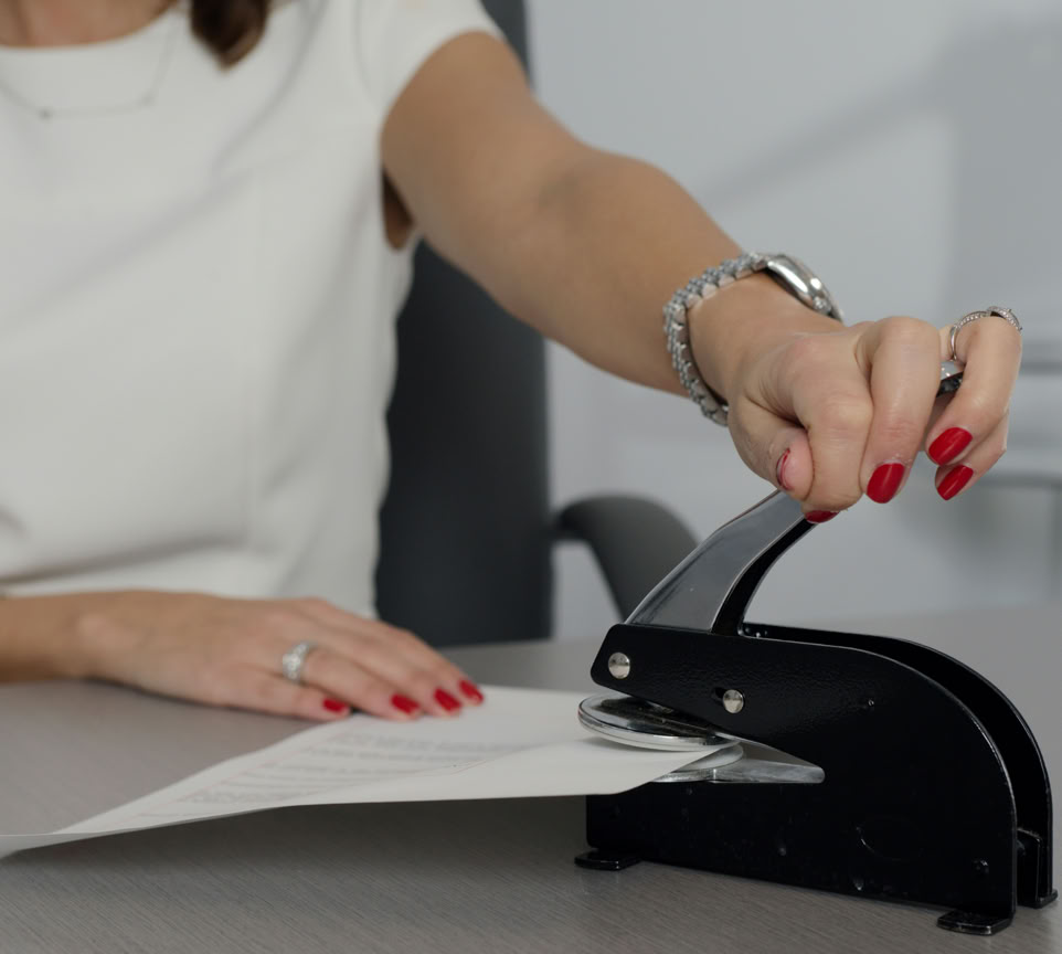 Young woman in a brown blazer signing documents at a table in a stylish office.